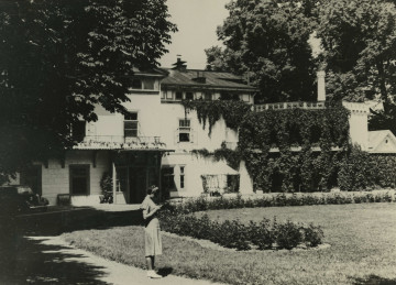 Na zdjęciu znajduje się kobieta stojąca w ogrodzie przed pałacem.