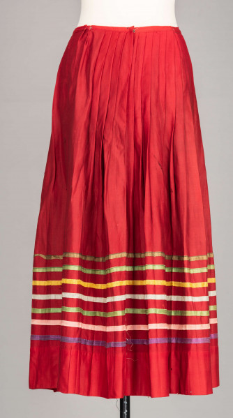 E/516/MRK/ML - Spódnica krakowska. Wykonana z wełenki, kolor czerwony. W dolnej czesci spódnica ozdobiona różnokolorowymi tasiemkami, sztuk 7. Przy oszewce lekko marszczona.