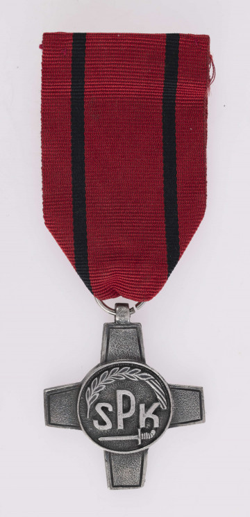 H/2463/MRK/ML - Odznaką jest krzyż bity w białym metaluo obramowanych ramionach, w środku okrągła tarcza z napisem SPK poniżej miecz, u góry otokowo kłos, wstążka czerwona z 2 czarnymi paskami.