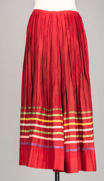 E/516/MRK/ML - Spódnica krakowska. Wykonana z wełenki, kolor czerwony. W dolnej czesci spódnica ozdobiona różnokolorowymi tasiemkami, sztuk 7. Przy oszewce lekko marszczona.