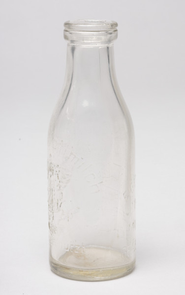 butelka po mleku - Ujęcie z boku; Butelka po mleku o pojemności 0,5 litra z przezroczystego szkła. Butelka z krótką szyjką i grubym kołnierzem dookoła wylewu.