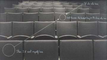 Z cyklu Rehearsals for Adulthood (If she seats here...) - ujęcie z przodu; Czarno-biała fotografia pustych, złożonych krzeseł na widowni sali teatralnej lub kinowej (7 rzędów). Diagonalnie, od lewego dolnego do prawego górnego rogu narysowane białym tuszem 3 kółka: 3 cm średnicy na oparciu siedzenia w lewym dolnym rogu, 1,5 cm śr. na krześle w 3 rzędzie od dołu, na prawo od osi fotografii, i trzecie, małe kóleczko na siedzeniu skrajnym po prawej stronie w przedostatnim rzędzie. Kółka te łączą strzałki (skierowane do środkowego kółka) i tekst napisany białym tuszem, pismem odręcznym, w j.angielskim: od kółka górnego do środkowego: 