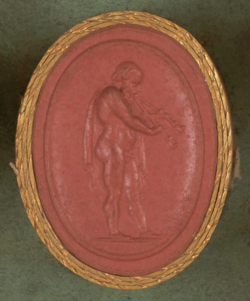 czerwona owalna gemma w grubym złotym obramowaniu; nagi starszy mężczyzna z peleryną zarzuconą na lewe ramię gra na podwójnym flecie (aulosie); postać widoczna jest z prawego boku, ma średniej długości włosy, wysokie czoło i brodę 