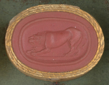 czerwona owalna gemma w grubym złotym obramowaniu, posta młodego lwa szykującego się do skoku, widziana z lewego profilu