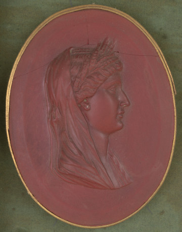 czerwony wycisk owalny ze złotym obramowaniem; prawy profil popiersia kobiety, kobieta na głowie ma wieniec z kłosów i chustę opadającą na tył głowy; u góry gemma pęknięta