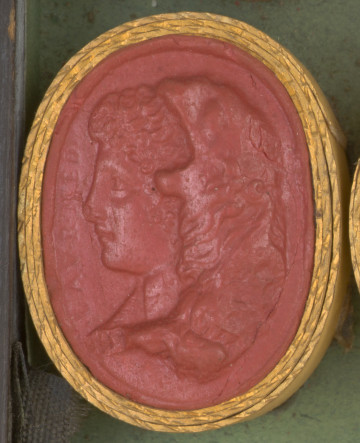 czerwona owalna gemma w grubym złotym obramowaniu, lewy profil kobiety z kręconymi włosami i lwią skórą na głowie; czubek nosa uszkodzony; z przodu wzdłuż profilu w otoku napis: LAV.R.MED