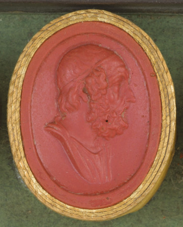 czerwona owalna gemma w grubym złotym obramowaniu; prawy profil starsego mężczyzny z kręconymi włosami zakrywającymi uszy i gęstą brodą, na głowie opaska, widoczny też fragment tuniki