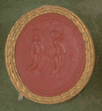 czerwona owalna gemma w grubym złotym obramowaniu; dwa nagie putta widziane z prawego profilu, bawiące się z wyciągniętymi do góry rękoma, jedno z nich w prawej ręce niesie tyrs, w tle widoczne draperie z materiału