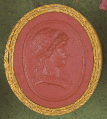 czerwona owalna gemma w grubym złotym obramowaniu; prawy profil młodzieńca z długimi włosami spiętymi u góry opaską, poniżej widoczny fragment szaty