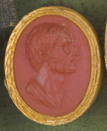 czerwona owalna gemma w grubym złotym obramowaniu; prawy profil mężczyzny w średnim wiekui, z krótkimi, lekko pofalowanymi włosami i krótką brodą, widoczny fragment tuniki