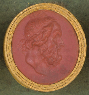 czerwona owalna gemma w grubym złotym obramowaniu; prawy profil starszego mężczyzny z długą kręconą brodą i długimi kręconymi włosami częściowo upiętymi cienką opaską