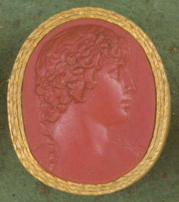 czerwona owalna gemma w grubym złotym obramowaniu; prawy profil popiersia młodego mężczyzny z krótkimi, kręconymi włosami i w wieńcu laurowym na głowie, z którego zwieszają się na ramiona dwie skręcone wstążki