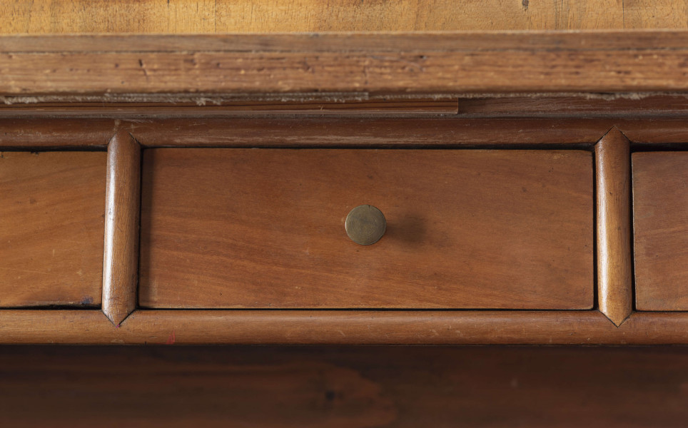 Biurko przyścienne na sześciu nóżkach graniastych zbieżnych. W części dolnej prostokątny prześwit zamknięty tylną ścianą. Po jego bokach po dwie szuflady, powyżej jeszcze trzy. Część górna ćwierćcylindryczna zamykana żaluzją chowaną pod górna płytą powyżej pięciu szufladek, boki zdobione plastycznym ornamentem cekinowym. Lico pokryte fornirem z intarsją ramkową i wzorem arkadkowym. Blat wyłożony skórą cielęcą. Uchwyty szuflad zewnętrznych i żaluzji to nałożone okucia okrągłe z tarczą, szufladki w części górnej mają uchwyty okrągłe z gładką główką.  