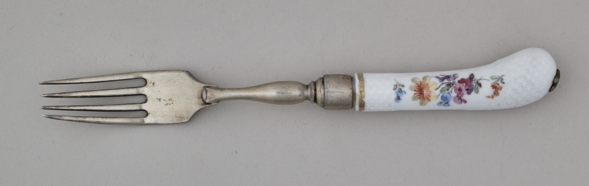Widelec śniadaniowy, czterozębny. Zęby wygięte, zwężające się przy zakończeniu. Trzonek z nakładką ze srebra złoconego z białej porcelany