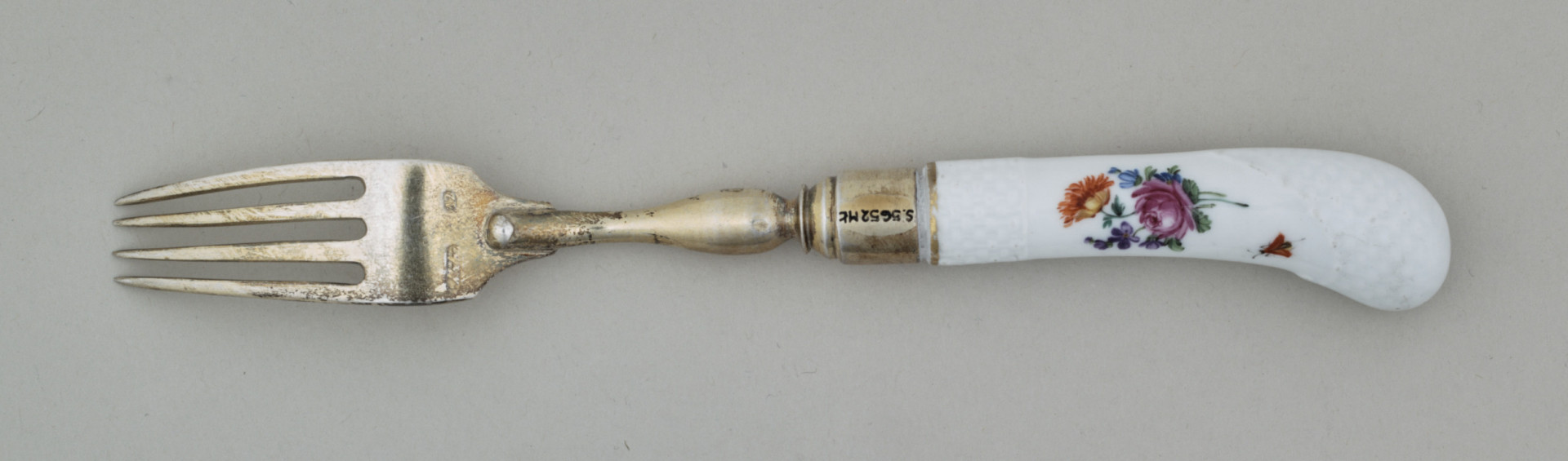 Widelec śniadaniowy, czterozębny. Zęby wygięte, zwężające się przy zakończeniu. Trzonek z nakładką ze srebra złoconego z białej porcelany