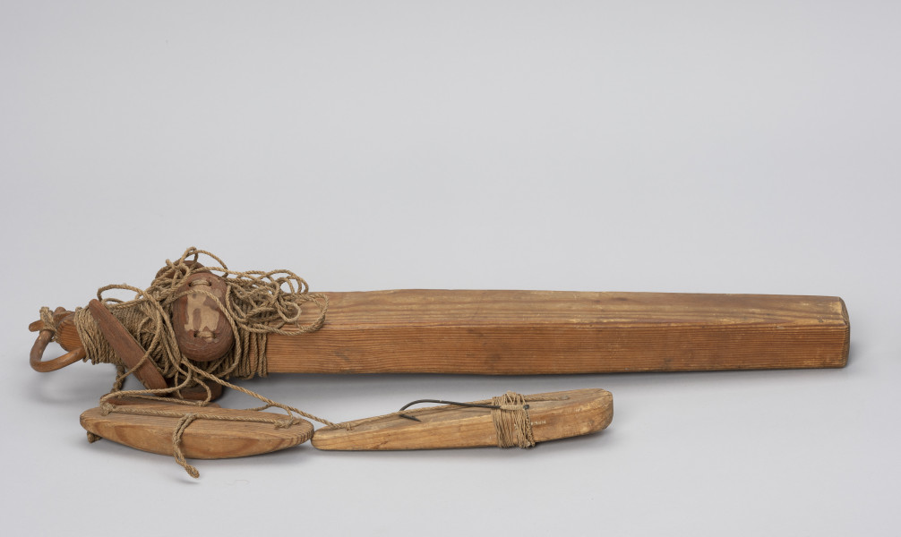 takla łososiowa z merkiem - Ujęcie z boku; Jednohaczykowa węda morska dryfująca służąca do połowu pojedynczych łososi znakowana merkiem FM.
Prezentowane narzędzie składa się z dużego, drewnianego pływaka (koby) i sznura oraz 7 pływaków - 2 wykonane z drewna i 5 z kory. Koba  zakończona jest haczykiem z przynętą w postaci żywej rybki, której brak, obciążona jest stożkowatym ciężarkiem.