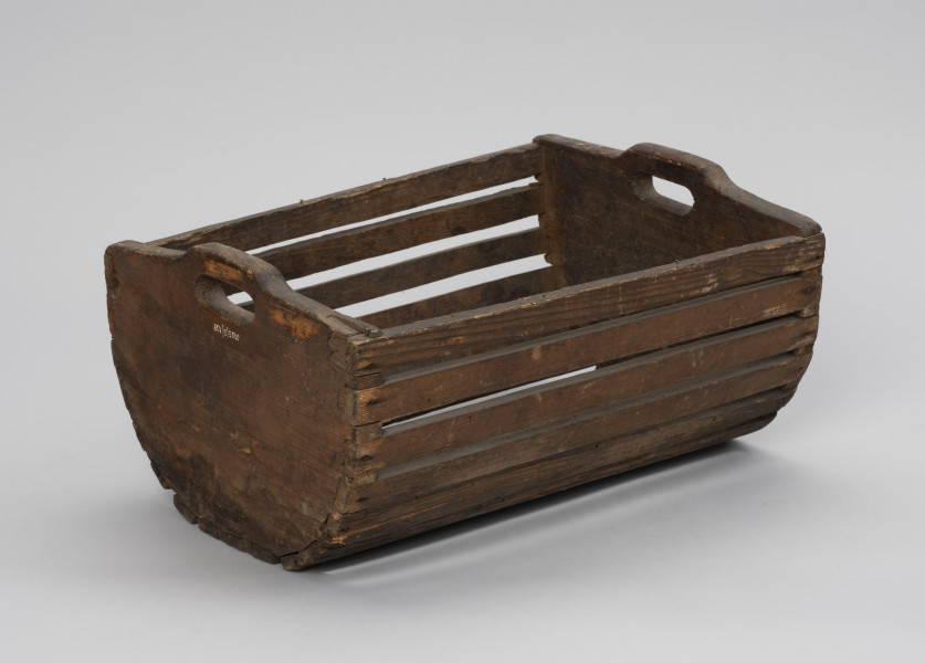 Skrzynka do przechowania i przenoszenia przynęty - Ujęcie ze skosu z lewej; Drewniana skrzynka w formie niecki, w przekroju poprzecznym – półkolista. Dłuższe boki i podstawę wykonana z płaskich klepek przytwierdzonych do krótszych, pełnych boków zaopatrzonych w uchwyty, Klepki do boków przybite gwoździkami.