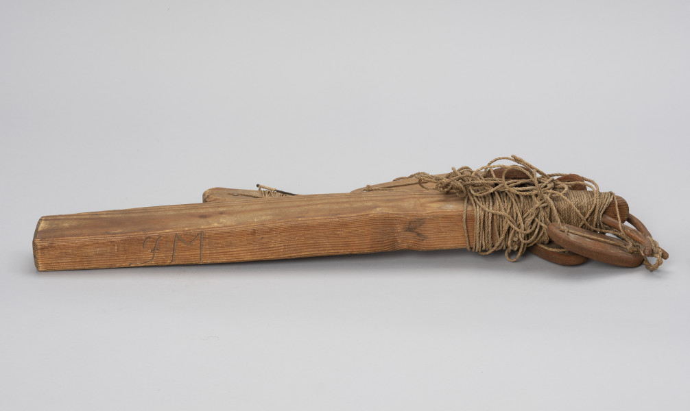 takla łososiowa z merkiem - Ujęcie z boku; Jednohaczykowa węda morska dryfująca służąca do połowu pojedynczych łososi znakowana merkiem FM.
Prezentowane narzędzie składa się z dużego, drewnianego pływaka (koby) i sznura oraz 7 pływaków - 2 wykonane z drewna  i 5 z kory. Koba  zakończona jest haczykiem z przynętą w postaci żywej rybki, której brak, obciążona jest stożkowatym ciężarkiem. Pływak - (koba) z drewna jest znakowany merkiem (znakiem własności) - inicjał FM ( być może są to inicjały darczyńcy).