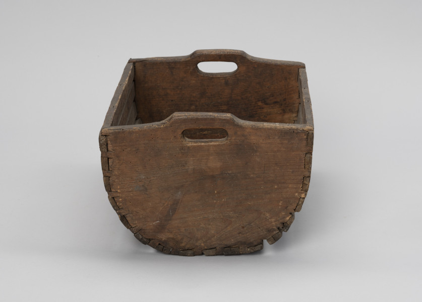 Skrzynka do przechowania i przenoszenia przynęty - Ujęcie z boku; Drewniana skrzynka w formie niecki, w przekroju poprzecznym – półkolista. Dłuższe boki i podstawę wykonana z płaskich klepek przytwierdzonych do krótszych, pełnych boków zaopatrzonych w uchwyty, Klepki do boków przybite gwoździkami.