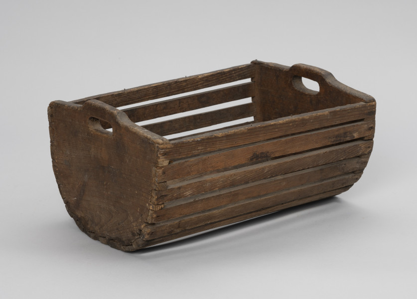 Skrzynka do przechowania i przenoszenia przynęty - Ujęcie ze skosu z lewej; Drewniana skrzynka w formie niecki, w przekroju poprzecznym – półkolista. Dłuższe boki i podstawę wykonana z płaskich klepek przytwierdzonych do krótszych, pełnych boków zaopatrzonych w uchwyty, Klepki do boków przybite gwoździkami.