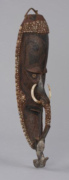 maska mai - Ujęcie z przodu skosem w prawą stronę. Drewniana maska antropomorficzna z długim nosem ozdobionym kłami dzikiej świni oraz gliniano-drewnianym mostkiem zwanym molot. Maska wydłużona i szczupła, stosunkowo wąska twarz z długim nosem, szerokimi ustami. Pod wydatnymi łukami brwiowymi znajdują się skośne oczy z zaznaczonymi powiekami, o kącikach skierowanych ku górze i gałkach ocznych w postaci muszli. Molot ma formę łukowatego uchwytu zaczynającego się poniżej nozdrzy, pod ozdobą nosa, a sięgającego do brody zakończonej ciosaną głową ptaka. Maska pokryta brązowymi barwnikami, wpadającymi w rdzawy i ciemnobrązowy kolor. Zdobiona wzorami geometrycznymi w postaci prostych i zakręcających linii (jest to prawdopodobnie forma tatuażu). Całość mai otoczona została czerwoną gliną w której umieszczono muszle, m.in. nossa i kauri (porcelanki). W ten sposób zaznaczono również policzki, opaskę nad czołem oraz górną część mostka. Na szczycie umieszczono pleciony uchwyt.