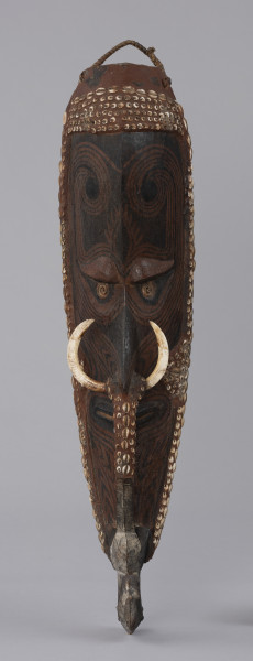 maska mai - Ujęcie z przodu; Drewniana maska antropomorficzna z długim nosem ozdobionym kłami dzikiej świni oraz gliniano-drewnianym mostkiem zwanym molot. Maska wydłużona i szczupła, stosunkowo wąska twarz z długim nosem, szerokimi ustami. Pod wydatnymi łukami brwiowymi znajdują się skośne oczy z zaznaczonymi powiekami, o kącikach skierowanych ku górze i gałkach ocznych w postaci muszli. Molot ma formę łukowatego uchwytu zaczynającego się poniżej nozdrzy, pod ozdobą nosa, a sięgającego do brody zakończonej ciosaną głową ptaka. Maska pokryta brązowymi barwnikami, wpadającymi w rdzawy i ciemnobrązowy kolor. Zdobiona wzorami geometrycznymi w postaci prostych i zakręcających linii (jest to prawdopodobnie forma tatuażu). Całość mai otoczona została czerwoną gliną w której umieszczono muszle, m.in. nossa i kauri (porcelanki). W ten sposób zaznaczono również policzki, opaskę nad czołem oraz górną część mostka. Na szczycie umieszczono pleciony uchwyt.