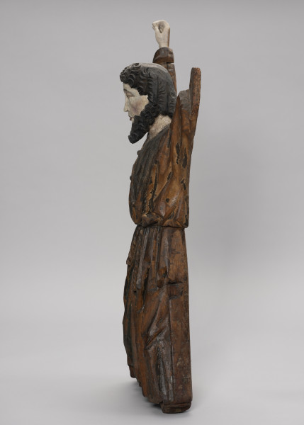 tłok pieczętny - Ujęcie z prawej; Męska figura w pozycji stojącej z uniesionymi rękami. Przedstawia młodego mężczyznę ubranego w długą obszerną tunikę spiętą w pasie sznurem. Światłocieniowe fałdowania szaty zostały oddane naturalistycznie, zgodnie z układem ciała. Podłużna twarz o wyrazistych kościach policzkowych oraz dużych ustach. Fryzura potraktowana dekoracyjnie. Tworzą ją ciemne, wyraziste spirale półdługich włosów, krótka grzywka i średniej długości broda. Figura przyścienna z tyłu płaska. Stopy i lewa dłoń nie zachowały się.