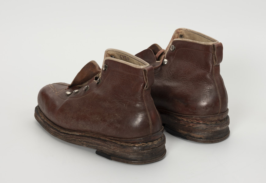 para trzewików - Ujęcie od tyłu ze skosu z lewej; Para damskich, brązowych, sznurowanych butów. Otwory na sznurówki zabezpieczone metalowymi obwódkami. Cholewka wykonana ze skóry licowej bydlęcej. To naturalna skóra, której zewnętrzna warstwa została poddana obróbce mechanicznej powodującej jej gładką fakturę. Między płaty skóry wszyte skórzane wzmocnienia na zapiętki. Podeszwy złożone z kilku warstw kruponu (najgrubszej części surowej skóry bydlęcej). Podeszwa zszywana. W wyniku zużycia skóry dosztukowane w latach późniejszych nowe warstwy kruponu z przodu podeszwy oraz fleki wykonane z gumy obuwniczej. Na flekach dodatkowe wzmocnienia metalowe. Buty noszą ślady dużej eksploatacji, uszkodzenia skóry przy górnym zakończeniu buta oraz po całości widoczna popękana skóra.