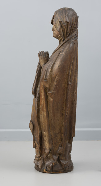 Matka Boska Bolesna z Chociwla - Ujęcie z prawej; Kobieca figura pełnoplastyczna, polichromowana. Przedstawia Marię stojącą frontalnie z dłońmi uniesionymi w geście modlitewnym. Ubrana jest w suknię o długich rękawach i szeroki modelowany światłocieniowo płaszcz otulający sylwetkę. Na głowie chusta. Pod spodem widoczna jest drobno marszczona podwika szczelnie okrywająca dekolt i szyję. Owalna twarz o smutnym wyrazie. Widoczne są drobne ubytki drewna w górnej partii chusty, na końcówkach palców dłoni i przy podstawie. Polichromia zachowana częściowo.