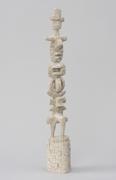 rzeźba; Światowid I - ujęcie tyłu ze skosu z lewej; Smukła, abstrakcyjna forma o jasnoszarej barwie na podstawie. Na szczycie antropomorficzna głowa o czterech twarzach umieszczona na słupie. Poniżej, jedna na drugiej, nieokreślone formy: belkowate; geometryczne, w tym zespolone ze sobą koła ustawione pionowo, pod kątem prostym względem siebie; formy księżycowate; przenikające się krzyżowo z trójnogiem u dołu. Powierzchnia gipsu niejednorodna: miejscami ze śladami szpachli i innych narzędzi, rysami; miejscami zaś opracowana szczegółowiej - wygładzona nieco w środkowej partii o geometrycznej formie z wkomponowanymi w nią dwoma płaskimi dyskami, na bokach których odciśnięto czworoboki z kołami w środku. Dwustopniowa podstawa w formie pionowo ustawionego walca o jajowatym przekroju i dokładnie opracowanej powierzchni, dającej wrażenie kamiennego muru.