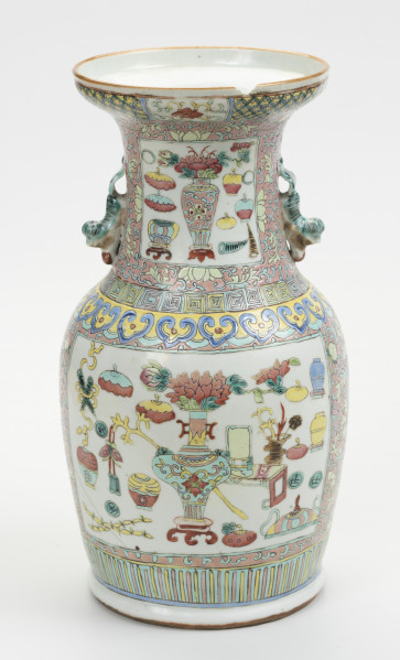 wazon typu famille rose - ujęcie z przodu; Porcelanowy wazon zdobiony wielobarwną dekoracją naszkliwną w pastelowych odcieniach z przewagą różu w typie famille rose. Kształt gruszkowaty, szyja szeroka zakończona rozszerzającym się wylewem, w którym widoczny jest z przodu półokrągły ubytek. Wazon bogato zdobiony licznymi motywami dekoracyjnymi. W jego górnej części znajdują się po bokach dwa uchwyty w formie stylizowanych lwów chińskich w kolorze pastelowej zieleni. Brzeg wylewu zdobiony dookolnie, z przodu kwiat lotosu o czerwonym kwiecie, żółtych i zielonych liściach na białym tle oraz zgeometryzowanym wzorem roślinnym w kolorach zielonym i różowym na żółtym tle. Szyję oddzielono od brzuśca biegnącymi dookolnie wzorami: ornamentem meandrycznym o różowej, żółtej i seledynowej barwie oraz znajdującym się pod nim motywem grzyba nieśmiertelności w niebieskim, żółtym, czerwonym i seledynowym kolorze. Brzusiec oraz szyję zdobią czworoboczne pola (rezerwy) o seledynowych bordiurach wypełnione tzw. motywem Stu Antyków (Hundred Antiques/Hundred Treasures) na białym tle. Pola wypełniają przedmioty i rośliny w dość nieformalnym układzie. Na szyi wyodrębnić można: rogi nosorożca, śliwki, wazon z peoniami na stojaku, różnorodne wazy (z przykrywkami oraz bez, na stojaku oraz bez), akwarium na stojaku, dyski z jadeitu, podwójną tykwę, z której unosi się smużka dymu oraz inne niezidentyfikowane przedmioty. Na brzuścu pokazano: śliwki, wazę z kwiatami na stojaku, akwarium na stojaku, parę skrzyżowanych rogów nosorożca, toaletkę z lustrem, różnorodne wazy, donicę z miniaturową rośliną na stojaku, naczynie na wysokim stojaku oraz inne niezidentyfikowane przedmioty i rośliny. Dół wazonu ozdobiony dookolnie geometrycznym motywem w postaci pionowych żółtych i różowych pasków na seledynowym tle.