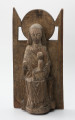 Tronująca Madonna z Dzieciątkiem - Ujęcie z przodu; Niewielka figura tronującej Marii z dzieciątkiem o zwartej bryle, przytwierdzona do wysokiego zaplecka o geometrycznym zwieńczeniu, polichromowana. Rzeźba w typie Sedes Sapientiae ukazuje frontalnie siedzącą na tronie Marię w sztywnej, wyprostowanej pozie z dzieckiem w wieku chłopięcym usytuowanym bokiem, w pozycji siedzącej, ponad jej lewym kolanem. Długa suknia i płaszcz Marii oraz tunika Jezusa gładko przylegają do ciał postaci tworząc nieznaczne, schematyczne draperie w partii nóg. Między goleniami Marii tkanina układa się w charakterystyczne trójkątne fałdy o ostrych krawędziach. Hieratyczne pozy postaci przełamuje gest dłoni matki przytrzymującej syna oraz prawa ręka chłopca wyciągnięta wysoko i ułożona na piersi matki. Głowa Marii osadzona na sztywnej, szerokiej szyi okryta chustą ułożoną w tylnej partii na kształt welonu sięgającego do ramion. Twarz pociągła, owalna, zastygła w pozbawionym emocji wyrazie. Symetryczna fryzura chłopca z falujących włosów sięga poniżej uszu. Zwieńczenie gładko opracowanego zaplecka tworzy kolisty nimb za głową Marii flankowany trójkątnymi sterczynami oparcia tronu. Rzeźba opracowana jako przyścienna. Brak prawej dłoni Marii. Powierzchniowe ubytki drewna i otwory po drewnojadach. Polichromia zachowana szczątkowo.