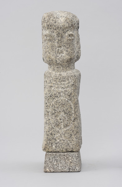 rzeźba; Polelum - ujęcie z przodu; Monolityczna, antropomorficzna pionowa forma o cechach ludzkich zredukowanych do prostopadłościennego korpusu i osadzonej na krótkiej szyi głowy. Głowa o miękko zaznaczonych rysach twarzy, wydobytych negatywowym szlifem powierzchni wokół nosa, oczu, ust i policzków, który nakreśla także linię fryzury. Korpus ozdobiony rytem owalu, skierowanej w górę strzały oraz trzech poziomych linii powyżej. Figura ustawiona na nieco szerszym, kamiennym postumencie.