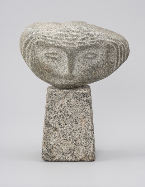 rzeźba; głowa - Ujęcie z przodu; Szeroka, spłaszczona, bliska owoidalnej głowa dołem lekko wydłużona, osadzona na kostce w kształcie ściętego ostrosłupa. Rysy twarzy: łuki brwiowe, nos, konturowo zaznaczone oczy, drobne usta – ciemniejsze, wydobyte przez delikatny, negatywowy szlif policzków i obszarów wokół oczu. Ryt ornamentalny włosów widoczny tylko na froncie skały, bezpośrednio wokół twarzy.