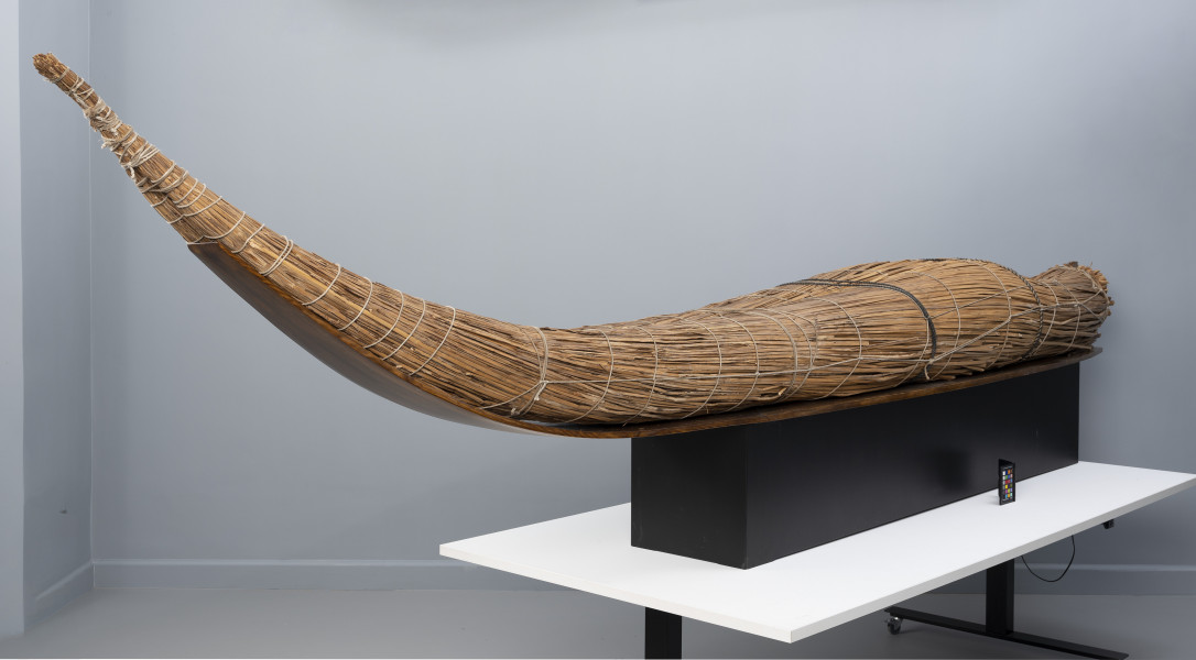 caballito de totora (łódź trzcinowa) - Ujęcie przodu ze skosu z lewej; Ponad czterometrowa łódź trzcinowa o naturalnym jasnobrązowym kolorze z wysoko zadartym ku górze długim, zwężającym się dziobem oraz grubą, płasko ściętą rufą. Kształtem przypomina gruby cios słonia. Została zbudowana z dwóch wiązek trzciny mocno skrępowanych przez poprzeczne wiązania. W ten sposób nadano łodzi pożądany, żeglowny kształt.