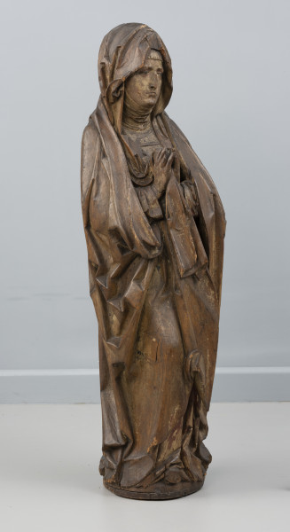 Matka Boska Bolesna z Chociwla - Ujęcie ze skosu z lewej; Kobieca figura pełnoplastyczna, polichromowana. Przedstawia Marię stojącą frontalnie z dłońmi uniesionymi w geście modlitewnym. Ubrana jest w suknię o długich rękawach i szeroki modelowany światłocieniowo płaszcz otulający sylwetkę, którego krawędź podłożoną pod prawym przedramieniem Marii opada z przodu szeroką trójkątnie zakończoną fałdą. Na głowie chusta osuwająca się na skronie zebrana jednym końcem pomiędzy dłonie. Pod spodem widoczna jest drobno marszczona podwika szczelnie okrywająca dekolt i szyję. Owalna twarz o smutnym wyrazie z ustami i oczami o opadających kącikach. Figura wewnątrz wydrążona. Z tyłu wzdłuż pleców i partii nóg długi prostokątny ruchomy element zakrywający otwór po wydrążeniu rzeźby, o powierzchni dopasowanej do fałdowań płaszcza. Widoczne są drobne ubytki drewna w górnej partii chusty, na końcówkach palców dłoni i przy podstawie. Polichromia zachowana częściowo.