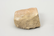 cegła szamotowa - Ujęcie z prawej; Prostopadłościenna cegła z jasnej glinki szamotowej. Widoczna strona obtłuczona. Cegła niejednolita, ziarnista.