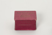 pudełko jubilerskie - Ujęcie z przodu; Małe, prostopadłościenne pudełko na biżuterię, z twardej tektury w kolorze amarantowym, delikatnie prążkowane. Pudełeczko otwierane uchylnie. Na wieczku napis czcionką w kolorze złotym: Rud. Kunstmann Juwelier Stettin Paradeplatz 12.