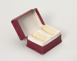 pudełko jubilerskie - Ujęcie przodu ze skosu z lewej; Małe, prostopadłościenne pudełko na biżuterię, z twardej tektury w kolorze amarantowym. Pudełeczko otwierane uchylnie – na widocznym ujęciu otwarte.