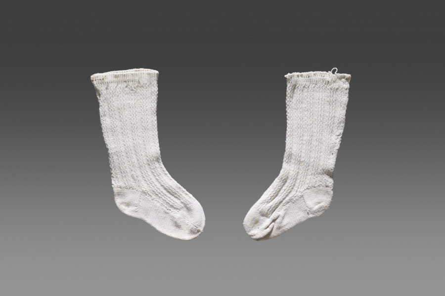 Para skarpet dziecięcych w kolorze białym/écru z widocznym ozdobnym ściegiem w formie trzech biegnących pionowo równoległych linii w równych odstępach. Wzdłuż górnej krawędzi wąski ściągacz. W części podeszwy oraz palców brak zdobienia.