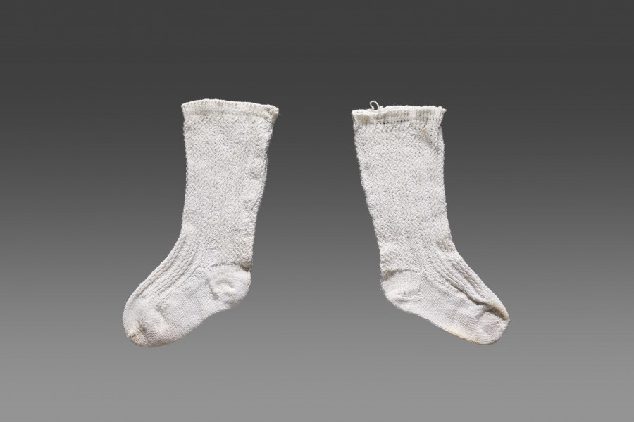 Para skarpet dziecięcych w kolorze białym/écru z widocznym ozdobnym ściegiem w formie trzech biegnących pionowo równoległych linii w równych odstępach. Wzdłuż górnej krawędzi wąski ściągacz. W części podeszwy oraz palców brak zdobienia.