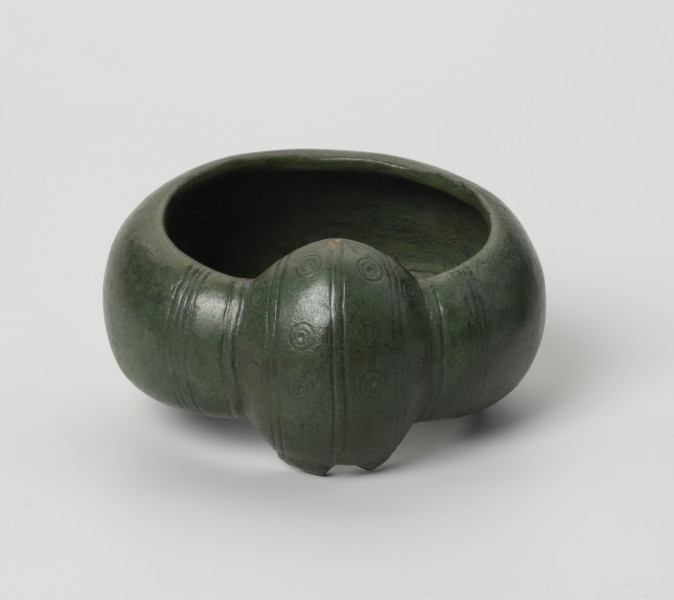 kopia bransolety nerkowatej z Kolkowa - Ujęcie z przodu; Bransoleta o szerokiej obręczy (5,9 cm), silnie wypukła. Jej brzegi są mocno zagięte do środka, co daje C-kształtny przekrój poprzeczny. Oba końce obręczy łączy duże zgrubienie, tzw. nerka. Końce i zgrubienie nerkowate zostały ozdobione pasmami zwielokrotnionych linii (3 pasma przypadają na zgrubienie, a 4 pasma na końce obręczy), które biegną poprzecznie w stosunku do obręczy. Pomiędzy pasmami na zgrubieniu nerkowatym znajduje się tzw. ornament oczkowy (współśrodkowe podwójne okręgi z centralnie usytuowaną kropką-wgłębieniem). Bransoleta ma zielony kolor.