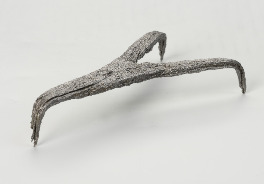 rak żelazny - Ujęcie tyłu ze skosu z prawej; Rak żelazny trójramienny z czworobocznej sztabki żelaznej z haczykiem na końcu każdego ramienia.