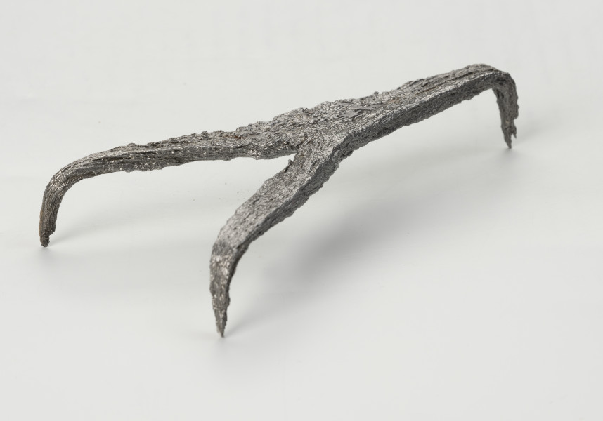 rak żelazny - Ujęcie przodu ze skosu z prawej; Rak żelazny trójramienny z czworobocznej sztabki żelaznej z haczykiem na końcu każdego ramienia.