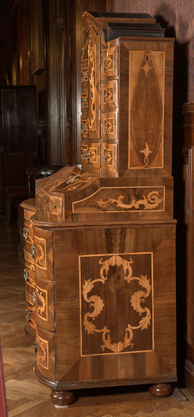 mebel o konstrukcji skrzyniowej, z wybrzuszonym frontem, na czterech kulistych nogach, wykonany z drewna iglastego, odłogowany (okleinowany) orzechem i intarsjowany jesionem (?) w motyw rocaili, część dolną mebla stanowi komoda o trzech szufladach; na niej sekretarzyk z uchylnym blatem-drzwiczkami ustawionym pod kątem i flankowanym dwiema szufladkami, wewnątrz dwa rzędy po cztery mniejsze szufladki; nastawa w formie szafki jednodrzwiowej z flankującymi ją szufladami (po cztery z każdej strony i pod drzwiczkami szafki