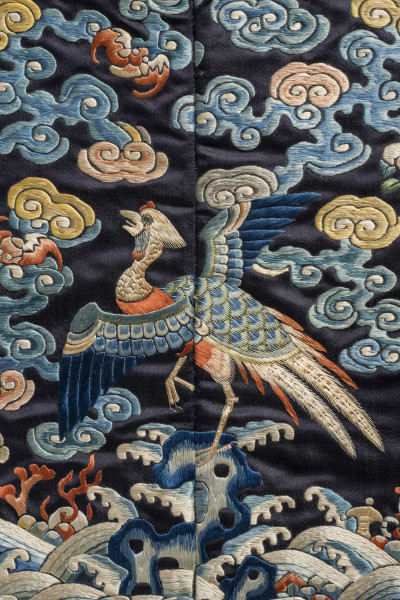 Na kwadracie jedwabiu wyhaftowany bażant z rozpostartymi skrzydłami stojący na skale. Wokół chmury. U dołu fale.