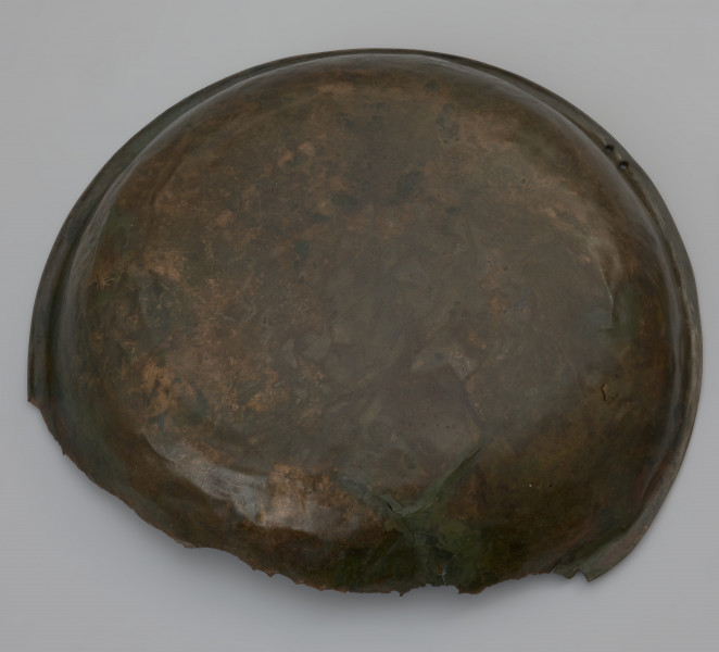 misa z rytem i tekstem - Ujęcie z dołu. Misa wykonana została ze stopu miedzi, z wąskim, wywiniętym, lekko pogrubionym brzegiem i płaskim dnem. Fragment misy uszkodzony bez obrzeża