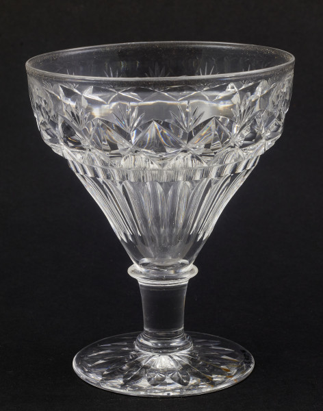 Stopa okrągła, nóżka krótka i szeroka, zakończona pierścieniem, na którym osadzona stożkowata czara. Spód stopy dekorowany płytkim szlifem o motywie wielopłatkowego kwiatka.