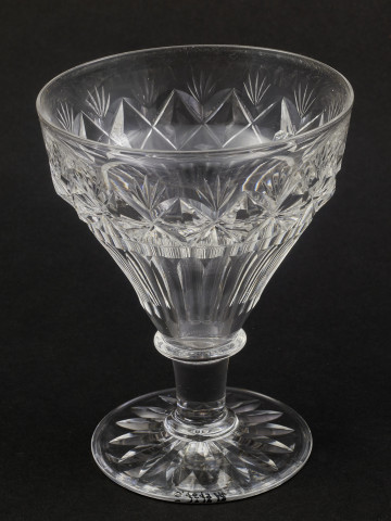 Kieliszek duży, wykonano ze szkła kryształowego
Stopa okrągła, nóżka krótka i szeroka, zakończona pierścieniem, na którym osadzona stożkowata czara. Spód stopy dekorowany płytkim szlifem o motywie wielopłatkowego kwiatka.
