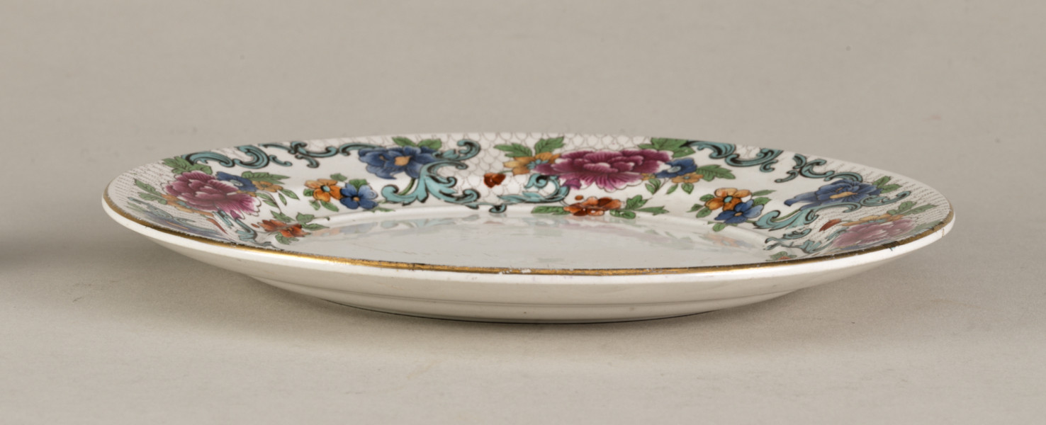 Mały, płytki talerzyk wykonany z białego fajansu. Stanowi podstawkę pod sosjerkę